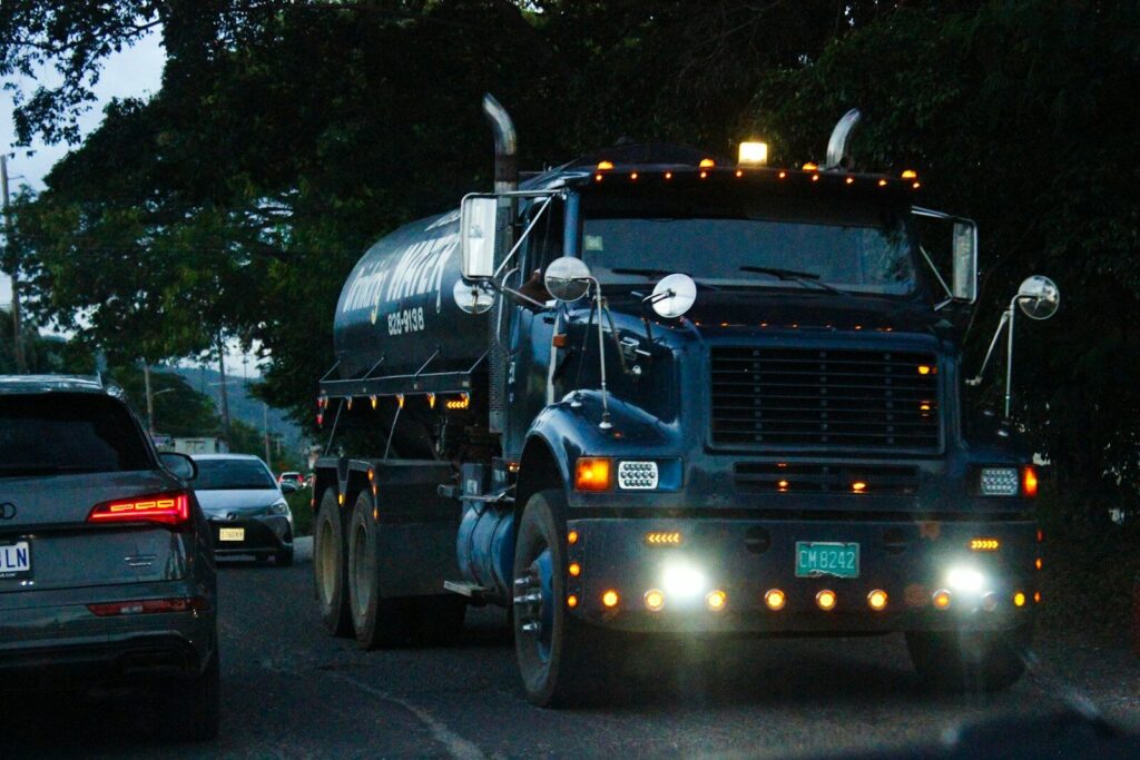 Blue tanker truck driving with lights on during dusk