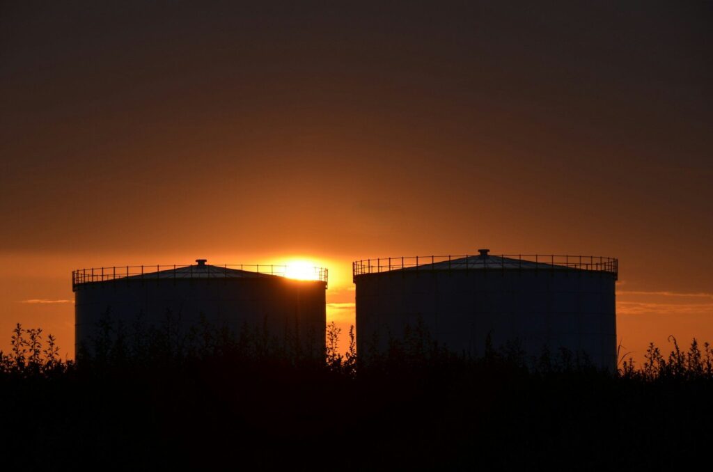 Sunset behind two large industrial storage tanks.